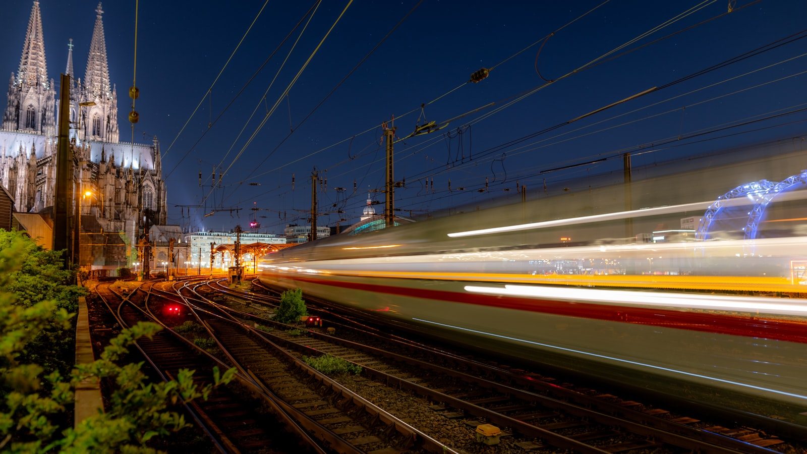 A high-speed train speeds past Cologne Cathedral at dusk in Germany